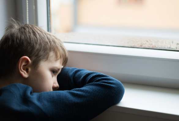 Sad child sits at window