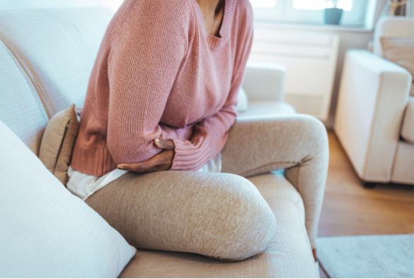 Woman sitting on couch holding stomach for comfort